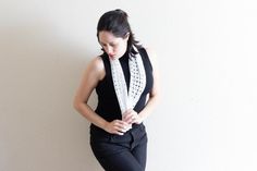 a woman standing in front of a white wall with her hands on her hips, wearing black pants and a crocheted scarf