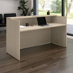 an office desk with a laptop on it in front of a large window and wooden floors