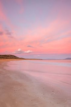 a pink sky over the ocean with footprints in the sand