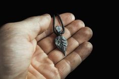 a hand holding a small pendant with a leaf on it's end and a black background