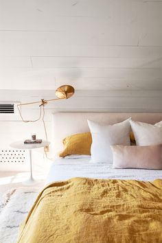 a bed with white and gold sheets in a bedroom next to a lamp on the wall