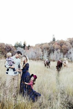 a family standing in tall grass with horses behind them