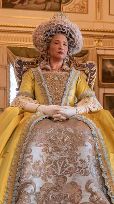 a woman sitting in a chair wearing a yellow dress and big curly hair with her hands on her hips