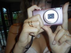 a woman holding up a pink camera to take a selfie with her ring in front of her face