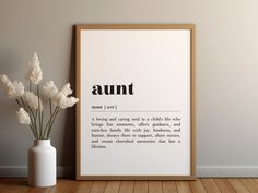 a white vase with some flowers in it next to a framed print that says,'annt '