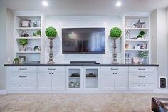 an entertainment center with white cabinets and black counter tops in a living room area that has carpeted flooring and built - in shelving