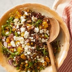 a bowl filled with vegetables and feta cheese next to a wooden spoon on top of a table