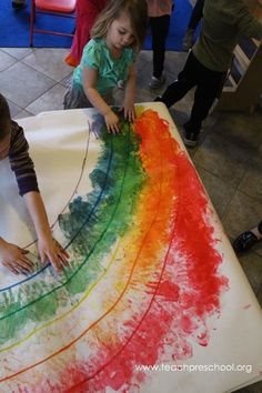 two young children are painting on a large piece of paper with colored crayons