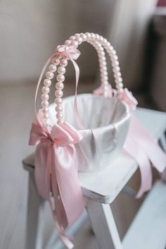 a white basket with pearls and a pink bow on it sitting on top of a wooden chair