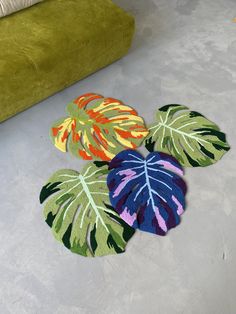 three rugs with leaves on the floor next to a green chair and couch in a living room