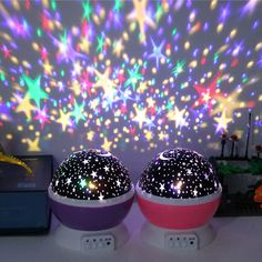 two colorful lights sitting on top of a white table next to a wall with stars painted on it