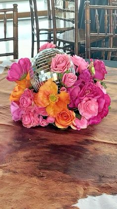 a bouquet of flowers sitting on top of a wooden table with chairs in the background