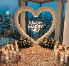 a large heart shaped arrangement with flowers and candles in front of a window that says will you marry me?