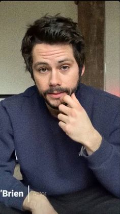 a man is sitting down with his hand on his chin and looking at the camera