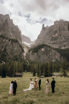 a group of people standing on top of a lush green field next to tall mountains