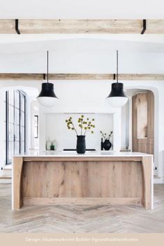 a kitchen with white walls and wood flooring is pictured in this image, there are black pendant lights hanging from the ceiling