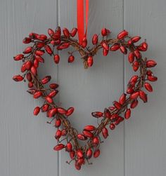 a heart shaped wreath hanging on the side of a building with red berries in it