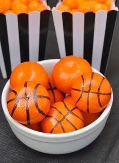 oranges in a white bowl with black and white striped paper bags behind them on a table