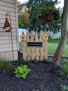 a wooden fence with flowers on it in front of a tree and some plants near by