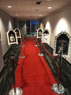 a long red carpeted hallway with pictures on the wall and barriers in between them