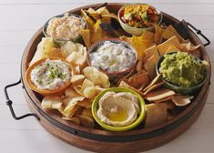 a platter filled with chips, guacamole and dips next to salsa