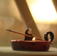 a small figurine sitting on top of a red bowl with a candle in it