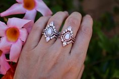 a woman's hand with two rings on it and flowers in the foreground