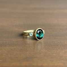 A bewitching teal tourmaline is elegantly positioned between a pair of beryls in this dazzling ring. 14k green gold Tourmaline 7mm x 9mm (1/4" x 3/8")Beryls 3mm (1/8") in diameterSapphires 1mm in diameter Green Tourmaline Ring For May Birthstone, Oval Tourmaline Ring For May Birthstone, 14k Gold Oval Emerald Ring With Three Stones, Green Emerald Three-stone Birthstone Ring, Oval Tourmaline Emerald Ring For Anniversary, Classic Oval Tourmaline Emerald Ring, Green Tourmaline Rings With Gemstone Accents, Green Tourmaline Rings With Accent Stones, Luxury Emerald Cut Emerald Ring With Gemstone Accents