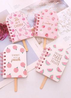 four pink notebooks with fruit on them are sitting next to an open planner book