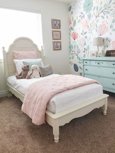 a white bed sitting in a bedroom next to a blue dresser and window with flowers on it