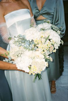 two bridesmaids holding bouquets of white and blue flowers in their hands,