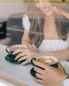 two people sitting at a table with cups of coffee in front of them, one holding the other's hand