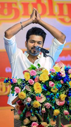 the man is giving a speech with his hands in the air and flowers on the table