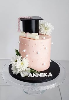 a pink cake with white flowers and a black top on a clear plate that says annika