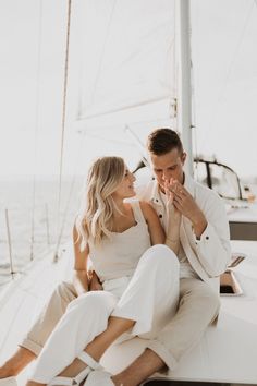 a man and woman sitting on the back of a sailboat in front of the ocean