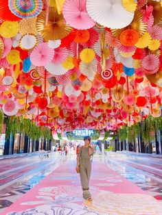 a woman walking down a runway covered in lots of colorful umbrellas hanging from the ceiling