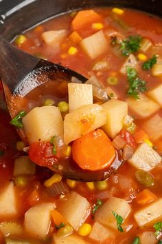 a spoon full of vegetable soup with corn and carrots on the side in a pot