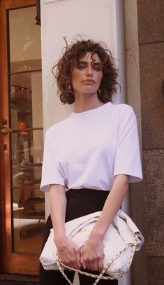 a woman with curly hair holding a white purse