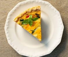 a slice of quiche on a white plate with a green leafy garnish