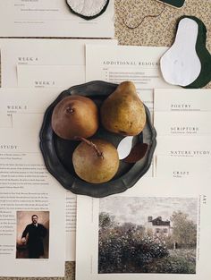 three pears in a bowl on top of an open book with other items nearby