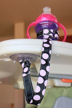 a pink and black polka dot pacifier on top of a baby seat with a purple cup