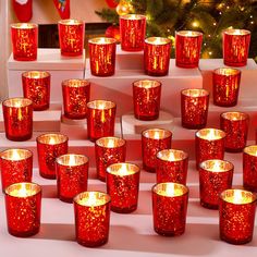 many red candles are lined up in front of a christmas tree with lights on it