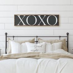 a bed with white sheets and pillows in front of a sign that says xoxo