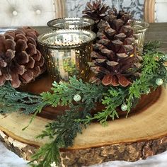 pine cones and evergreen branches are arranged on a wood slice with two votives