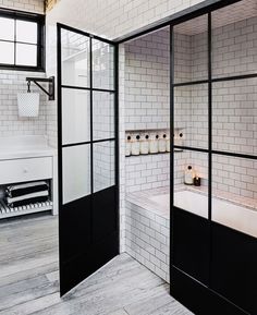 a bathroom with white brick walls and black glass doors that lead to the bathtub