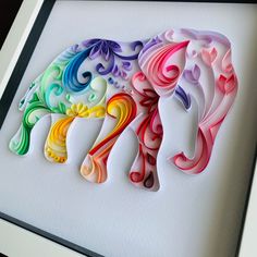 an elephant made out of colored paper sitting on top of a white surface next to a black frame