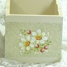 a white box with flowers painted on the front and sides, sitting on a lace covered surface