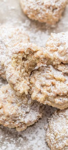 some cookies are covered in powdered sugar on top of a white surface with more cookies behind them