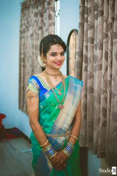 a woman in a green and blue sari standing next to a window with curtains