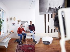 two men sitting on chairs in a room with a dog hanging from the ceiling and another man standing next to them